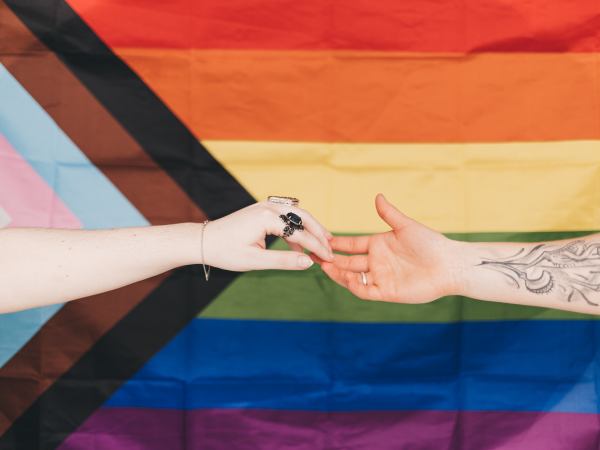 Two people reaching out to each other in front of a Progress Pride flag