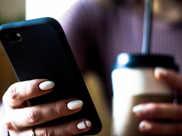 The hands of a person holding a phone and a cup of coffee
