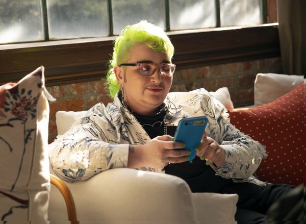 A genderqueer person using their phone on the sofa.