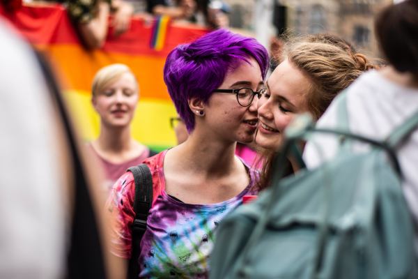 Two white queer people being affectionate in a crowd.
